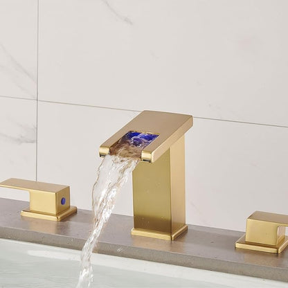 Gold bathroom faucet with water flowing against a light gray tiled wall.
