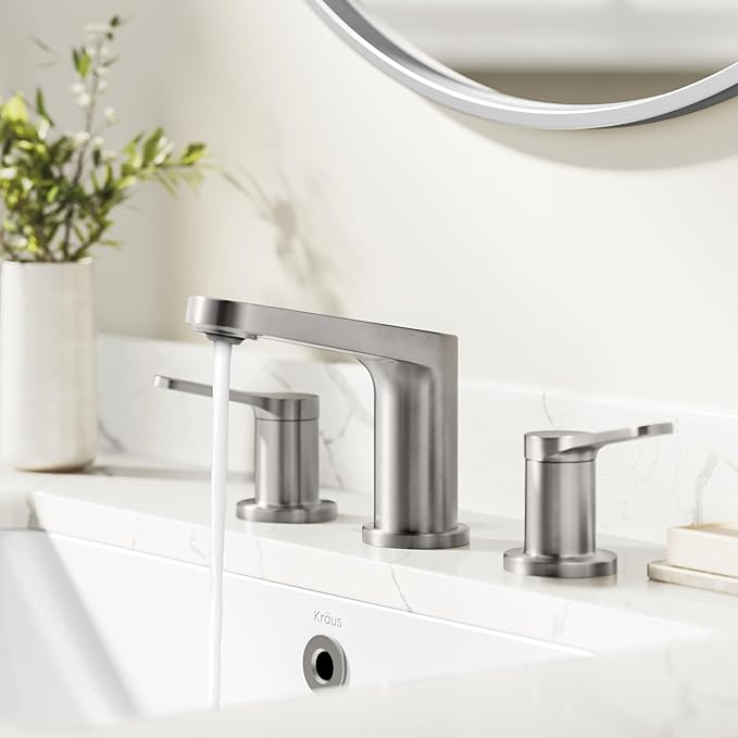 Bathroom faucet set on a white countertop with a mirror and plant in the background