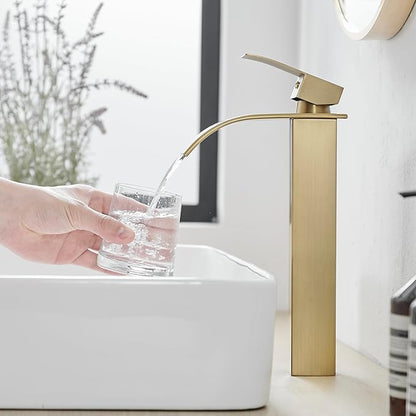 Gold faucet pouring water into a glass over a white sink.