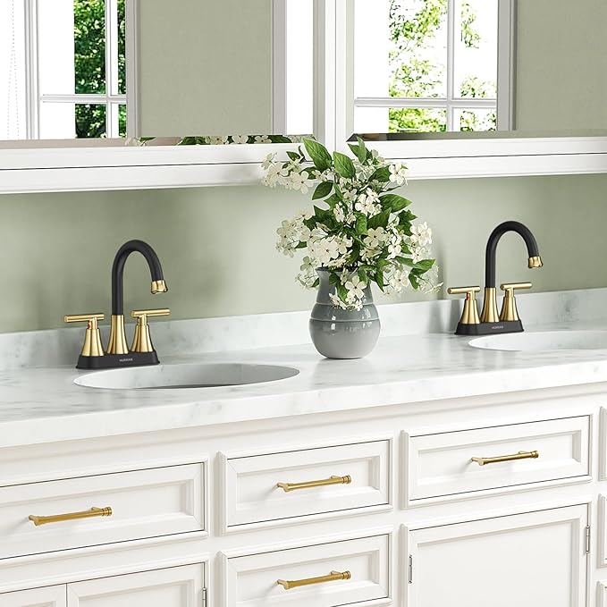 Bathroom vanity with white marble countertop, black and gold faucets, and a vase of flowers.